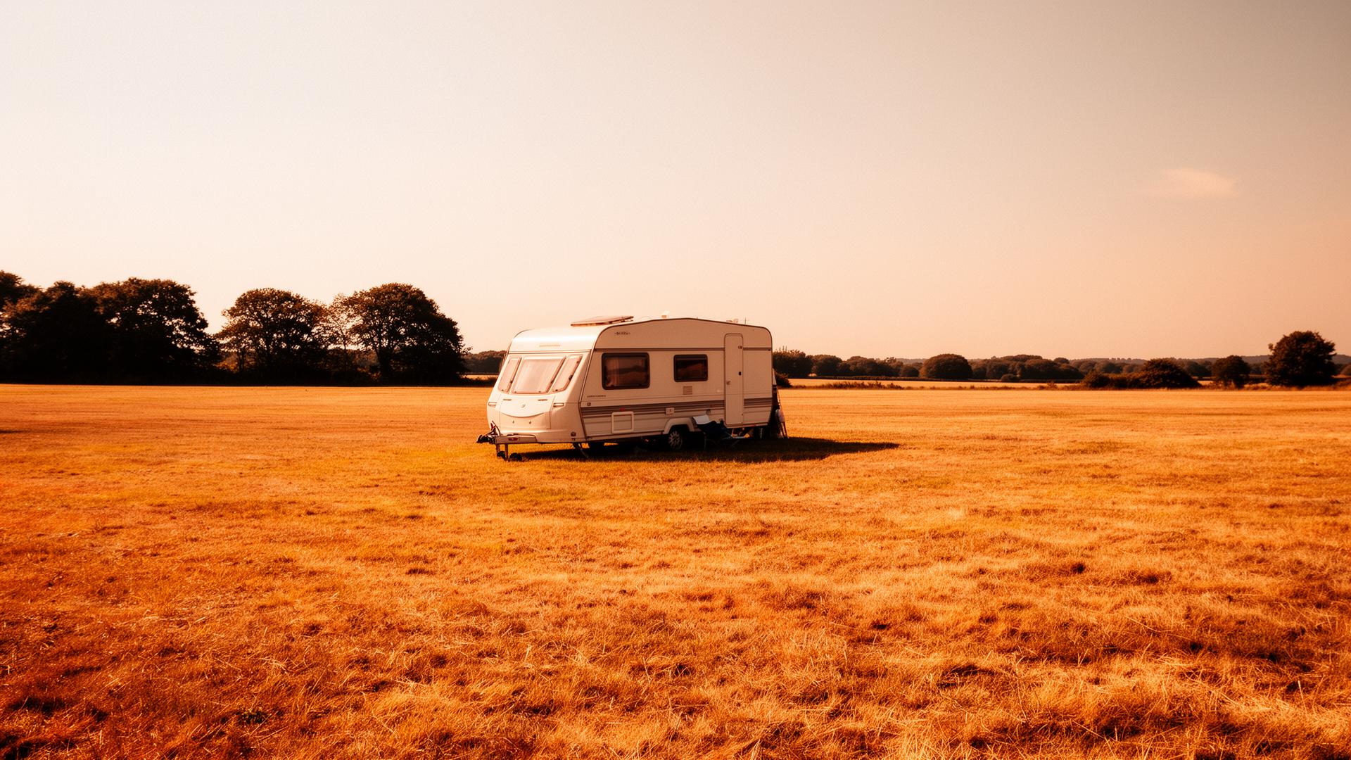 Eenzame caravan op een kaal, zonovergoten kampeerveld zonder schaduwbomen in de buurt.